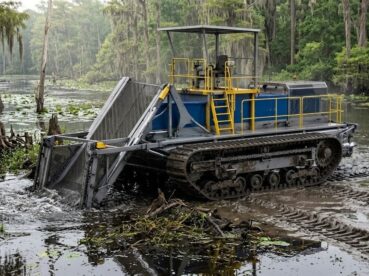 Amphibious harvester removing aquatic vegetation from shallow water and wetland areas